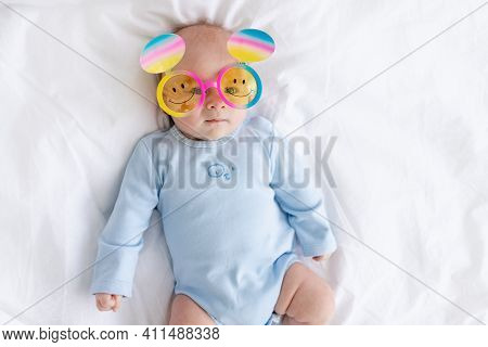 Baby Boy In Funny Glasses On The Bed, Holiday And Fun Concept