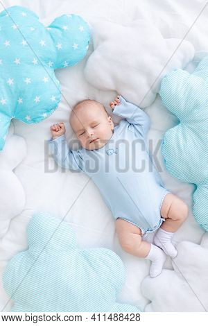 Baby Boy Sleeps On The Bed Lying On His Back Among The Pillows In Blue Pajamas, Healthy Newborn Slee