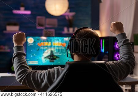 Excited Player With Headphones Making Winner Gesture While Playing Games On Computer At Gaming Home 