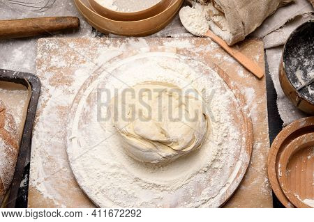 Kneaded Dough Of White Wheat Flour Lies On A Round Wooden Board, A Metal Bucket And A Wooden Rolling