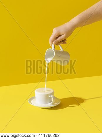 Woman Pouring Milk From A Jug, In Bright Light, Isolated On Yellow-colored Background. Milk Dripping