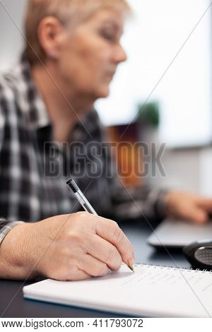Close Up Of Senior Business Woman Writing Notes On Notebook. Elderly Woman In Home Living Room Using