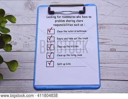 Text On Blue Clip Board With Pen On Wooden Desk. Finding Roommate Checklist