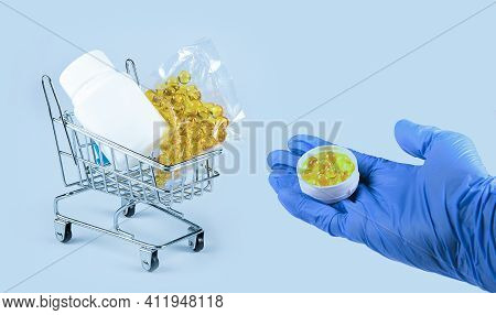 Hand In Blue Medical Glove Holding Round Box With Yellow Food Supplement Oil Filled Capsules Contain