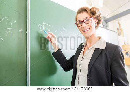 Teacher or docent writing with chalk on the board or  chalkboard or blackboard while math lesson in school class