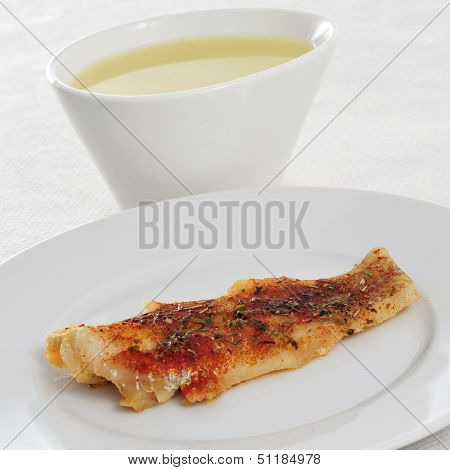 a bowl with consomme and a plate with a grilled hake fillet on a set table