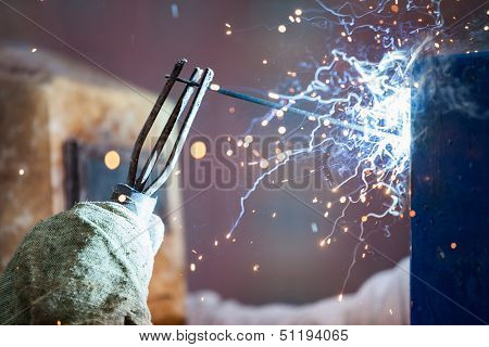 Heavy industry welder worker in protective mask hand holding arc welding torch working on metal construction