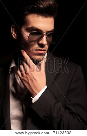 dramatic pensive young man in suit and sunglasses looking thoughtful on black background