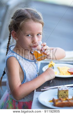 Adorable little girl having breakfast at outdoor cafe