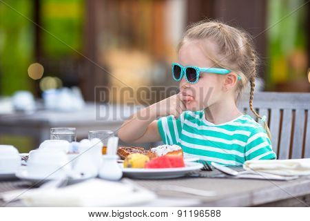 Adorable little girl having breakfast at outdoor cafe