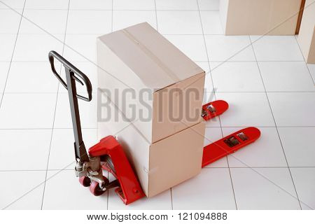 Fork pallet truck with stack of cardboard boxes indoors