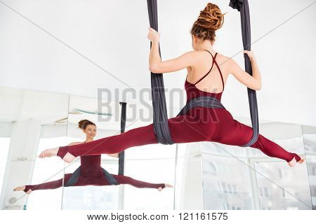 Back view of smiling pretty young woman doing twine using hammock on antigravity youga class