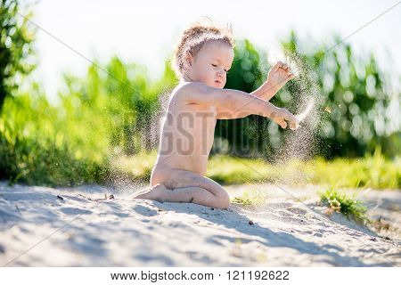 Little chubby toddler boy playing in the sandbox,  summer in Sunny weather. Throws sand