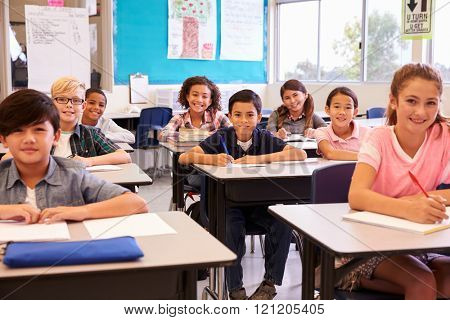 Smiling elementary school kids sitting at desks in classroom