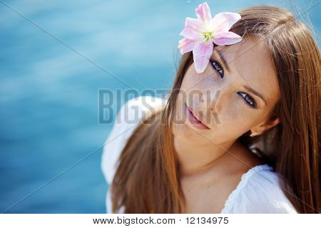 ภาพ Closeup ของผู้หญิงสวยคล้ำกับลิลลี่ในผมวางตัวเหนือทะเล