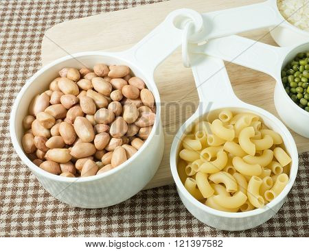 Foods High in Carbohydrate Raw Pasta Rice Peanuts and Mung Beans in Plastic Measuring Spoons.