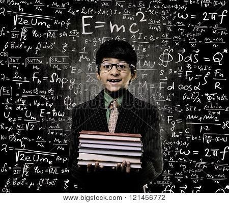 Cute Intelligent Little Boy Holding Book And Wearing Glasses Standing Before A Chalkboard Chemical Formulas Are Written On Board