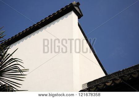 A white wall at Li Yuan Garden in the water town of Zhaojialou in Shanghai China against a blue sky.