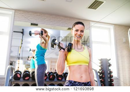 Two fit women in gym working out with weights