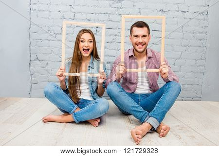 Cheerful couple in love sitting on the floor and holding wooden frames