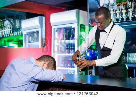 Drunk man sleeping with his head on bar counter while bartender making a drink for him