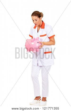 Young beautiful female doctor or nurse holding a piggybank