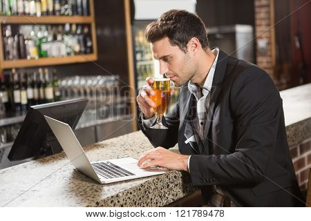 Handsome man using laptop and having a beer in a pub