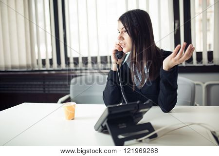 Young business woman calling and communicating with partners.Customer service representative on the phone.Cheerful secretary answering phone in her office and drinking coffee