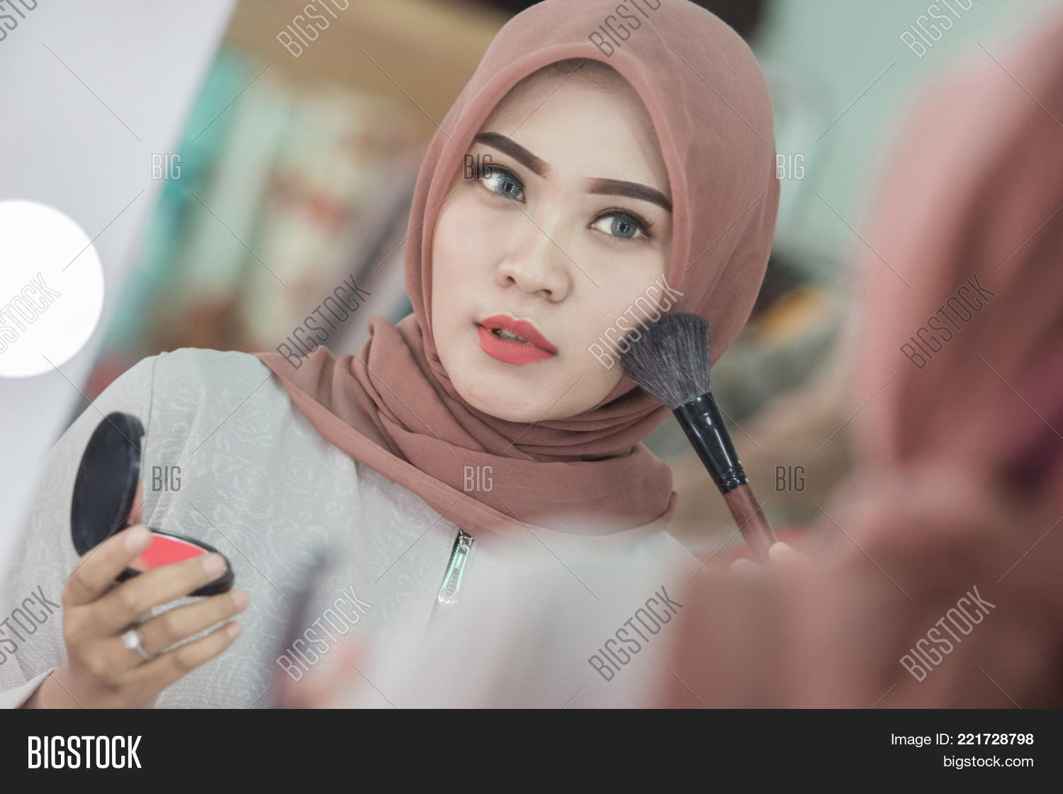 Beauty muslim woman with hijab applying makeup. Beautiful girl looking in the mirror and applying