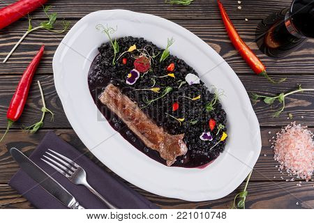 Meat with a garnish in white plate, top view. lamb with pearl barley with cuttlefish ink. Eastern cuisine. Wooden background