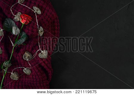 Brown knitted plaid and red rose on black background. Overhead view. Flat lay, top view. Copy space. Still life