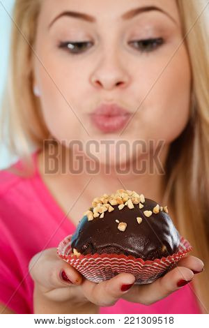 Diet, sweets, food concept. Woman holding delicious chocolate cupcake with peanut frosting about to take bite