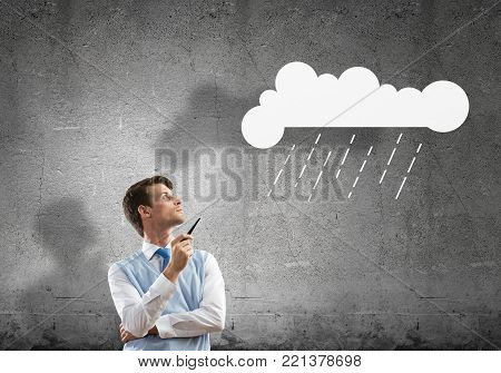 Horizontal shot of confident and young businessman in smart-casual wear smoking pipe while standing against gray dark wall on background.