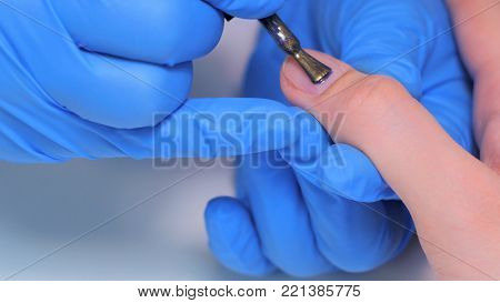 Professional beautician applying nail polish to female nail in a nail salon.