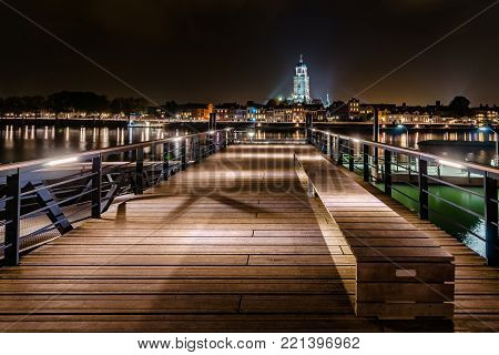 Deventer at night with view from a jetty over the river Ijssel. The tower of the Lebuinus church is towered above the beautifully lit cityscape.