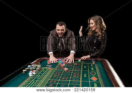 A man in a suit with a woman in a beautiful black dress playing roulette at the casino. Gambling. Casino. Roulette. Poker.