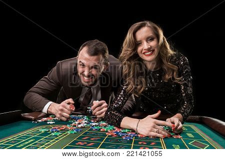 A man in a suit with a woman in a beautiful black dress playing roulette at the casino. Gambling. Casino. Roulette. Poker.