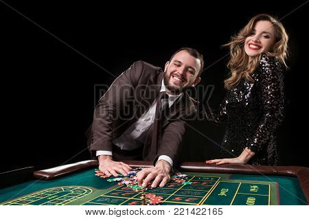 A man in a suit with a woman in a beautiful black dress playing roulette at the casino. Gambling. Casino. Roulette. Poker.