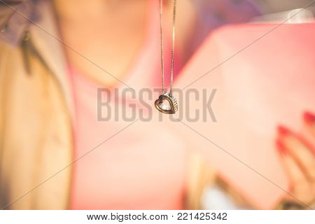 Young beautiful woman get a heart shape gold necklace gift from her boyfriend on Valentines Day. Closeup view.