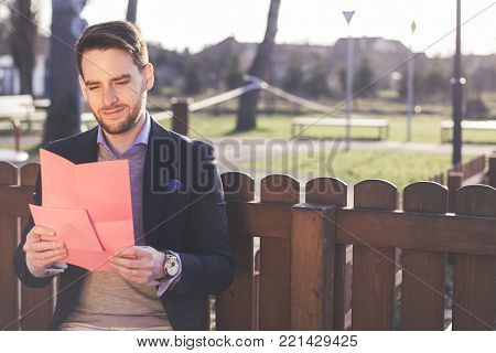 Handsome elegant man reading a love letter on Valentines Day at the park.