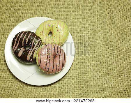 Flat lay Multicolored donuts on white dish brown color Hessian sackcloth woven background