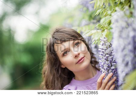 Portrait of a beautiful young brunette woman. A young woman is walking along the spring park. The girl is standing near the wisteria. Blooming park. Spring.