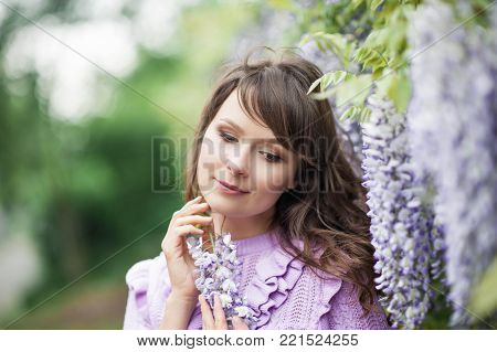 Portrait of a beautiful young brunette woman. A young woman is walking along the spring park. The girl is standing near the wisteria. Blooming park. Spring.