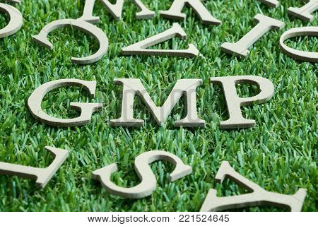 Wood letter in word GMP (Abbreviation from Good manufacturing practice) on artificial green grass wit English alphabet background