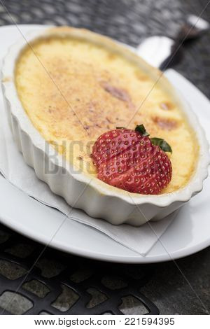Sweet and creamy custard dessert made of egg, milk and sugar topped with a sliced strawberry in a white plate
