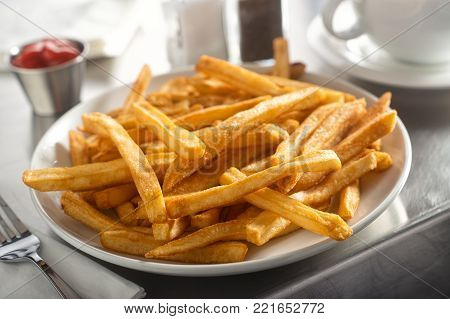 A plate of delicious crispy french fries served in a diner on a stainless steel countertop.