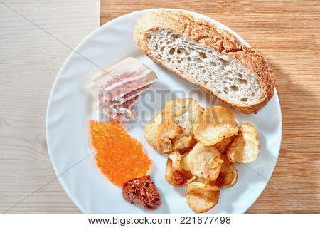 Tasty junk food. Greasy fried potatoes, bacon, red caviar, spicy sauce and white bread on a white plate. Russian snacking.