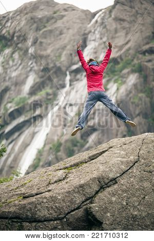 Happy woman jumping on rock in grey mountains, enjoying traveling and adventure.