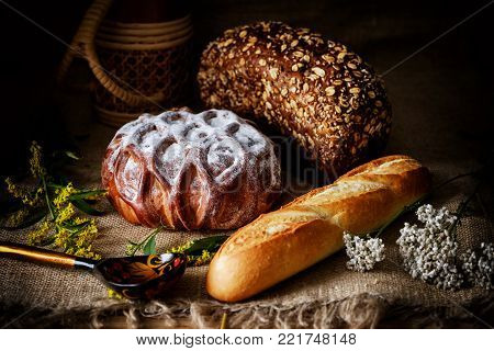 Sweet loaf of white bread powdered with sugar, brown bread, loaf of french bread on a dark rustic background.