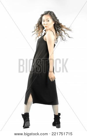full lenght portrait of asian woman in black dress and boots standing back and turning her face forvard with her hair develops